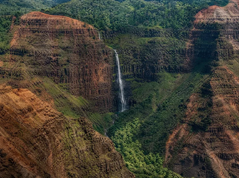 Waipoʻo Falls dropping roughly 800 feet into the red walls of Waimea Canyon, seen from the rim